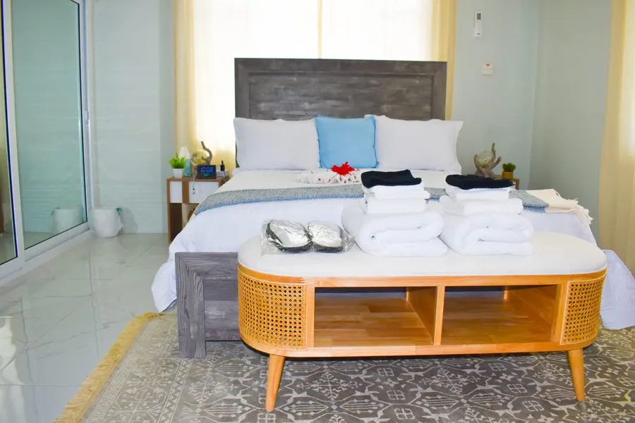 Main bedroom with a grey wood headboard, queen bed and rattan bench