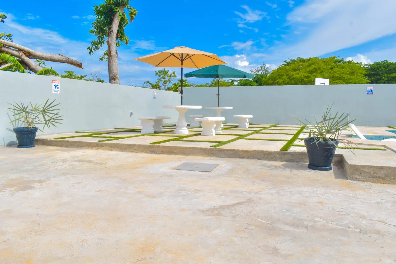 The walled pool terrace under a blue sky, with umbrellas, a stone table and loungers